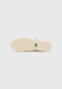 Sneaker sole in beige rubber with textured pattern. Features a green logo and accents in yellow and dark green. Flat design.