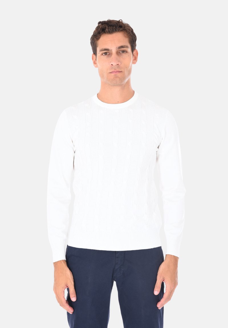 Maglione bianco in maglia con collo rotondo e maniche lunghe, realizzato in un tessuto morbido. Indossato con pantaloni blu navy.