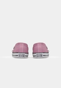 Ténis Converse All Star rosa com parte superior em lona, sola de borracha preta e branca, e duas tiras frontais para fecho. Logotipo na parte de trás é visível.