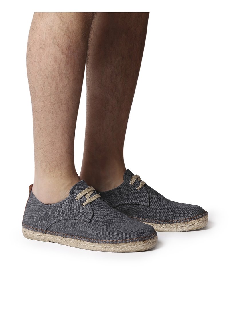 Scarpe in tela grigia con design arrotondato, lacci frontali e soletta in juta beige. La parte superiore presenta dettagli cuciti e una piccola linguetta sul tallone marrone.