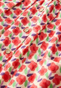 Korte mouwen stoffen shirt met een bloemenpatroon van rode bloemen, groene bladeren en paarse accenten, afgewerkt met beige knopen.