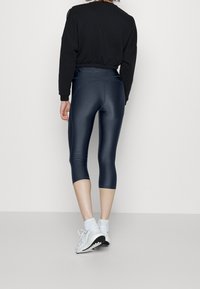 Laivastonsiniset, korkeavyötäröiset capri-leggingsit kiiltävällä pinnalla, yhdistettynä mustaan, lyhennettyyn svetariin. Valkoiset urheilukengät ja sukat viimeistelevät asun.