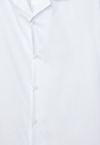 Camicia bianca con colletto classico, texture liscia e sei piccoli bottoni rotondi lungo la parte anteriore.