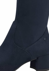 Bottines en suede bleu marine avec un talon bloc, présentant une texture lisse et un subtil détail de couture, conçues pour une silhouette ajustée.