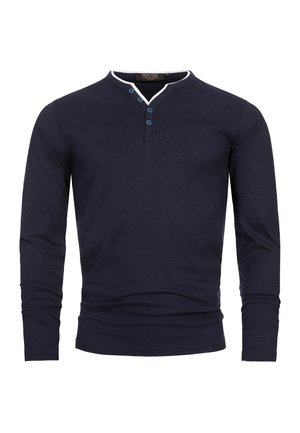 Chemise à manches longues bleu marine en coton, avec un col Henley doté de trois boutons bleus et une bordure de col blanche. Design minimaliste.