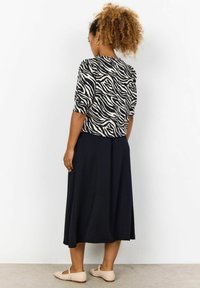 Sort og beige zebra print top med korte ærmer, parret med en lang sort nederdel og lyse beige flade sko. Glat stoftekstur.
