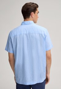 Lichtblauwe shirt met korte mouwen, gemaakt van gestructureerde stof met een kraag en details op de rug, zichtbaar van de achterkant.