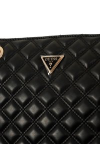 Borsa a tracolla in ecopelle trapuntata nera con logo GUESS metallico a forma triangolare. Motivo a rombi cucito con dettagli in metallo color oro.