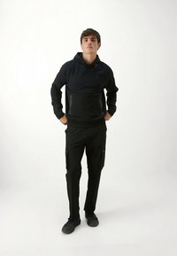 Črna jopa s kapuco in ujemajoče kavbojke s tovornim žepom. Jopa ima sprednji žep in vrvico za zategovanje. Hlače imajo stranske žepe in zoženo prileganje.