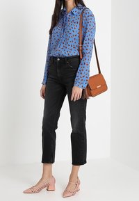 Camicia button-up azzurro chiaro con stampa floreale marrone, jeans neri a gamba dritta, scarpe con tacco a blocco perforate rosa e borsa a tracolla marrone.