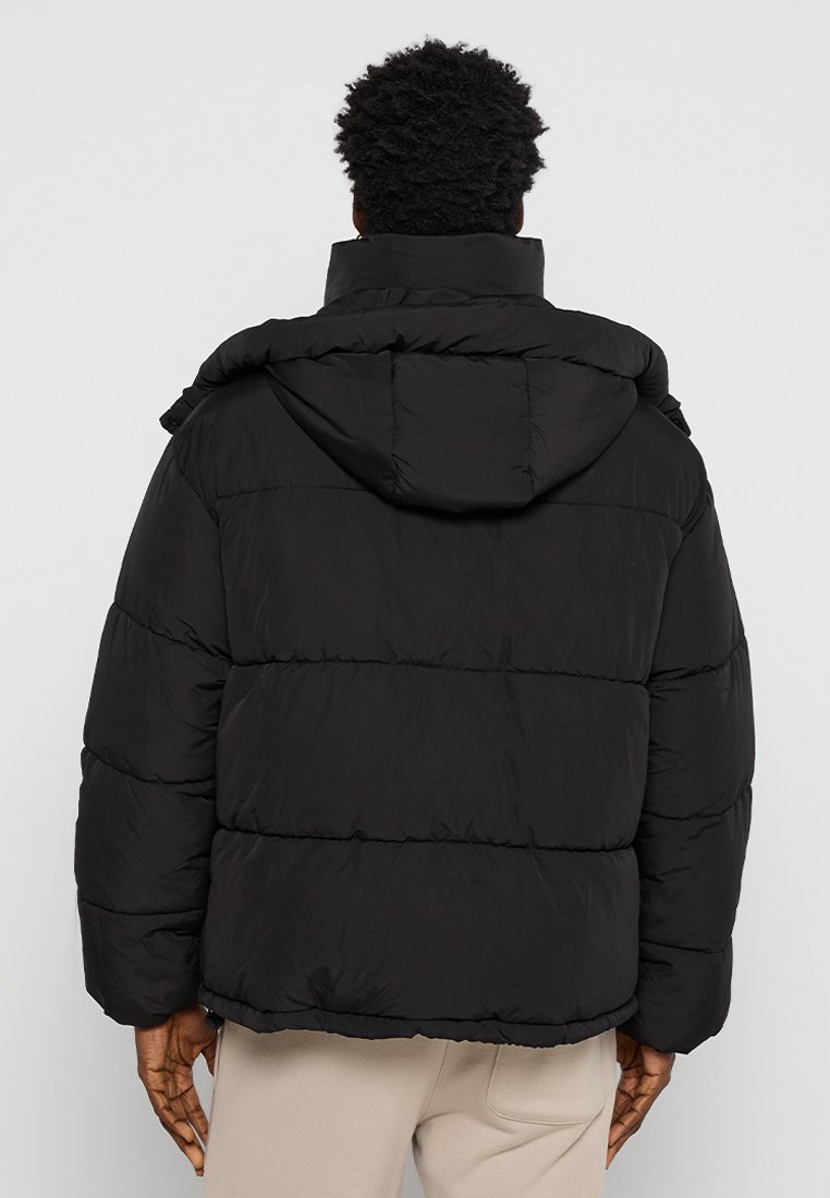 Czarna kurtka puchowa z kapturem, z pikowanym wzorem i luźnym krojem. Materiał ma gładką teksturę i jest ocieplony dla zapewnienia ciepła.