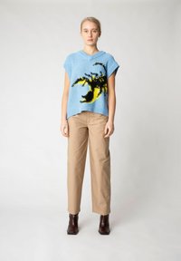 Blå stickad topp med en svart och gul grafisk design, kombinerad med beige vida byxor och bruna ankelboots.
