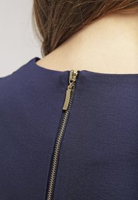 Granatowa bluzka z pionowym złotym zamkiem z tyłu, miękka w dotyku i z dekoltem crew.