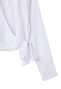 Camicia bianca avvolgente con maniche lunghe, caratterizzata da un dettaglio con legatura frontale e una texture in tessuto liscia e leggera. Il polsino è semplice e ordinato.