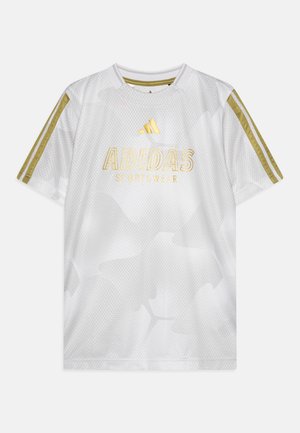 Valge Adidas spordiriiete T-särk, millel on meshtarud tekstuur, kuldsed detailid ja kolm kuldset triipu igal õlal. Selles on kirjas "ADIDAS SPORTSWEAR" kuldsete tähtedega.