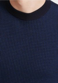Pull en maille bleu foncé avec un motif texturé, doté d'un col rond côtelé noir. Tissu doux avec une coupe ajustée.