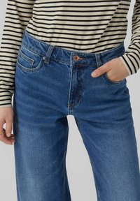 Blaue Denim-Jeans mit hoher Taille, Fünf-Taschen-Design und Knopfverschluss. Mit dezenten Ausbleichungen und geradem Beinschnitt. Oberteil mit weißen und schwarzen Streifen.