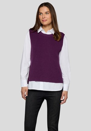 Lila gestrickte Weste mit rippenartiger Struktur, getragen über einem weißen Hemd, mit rundem Ausschnitt und ärmellosem Design. Gestylt mit dunkler Hose.