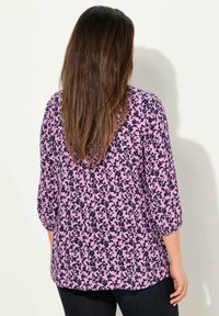 Blusa a maniche lunghe rosa con motivo floreale nero, in tessuto leggero, orlo rotondo e vestibilità rilassata. Progettata con maniche a tre quarti.
