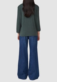 Un haut à manches longues vert foncé avec une coupe décontractée, associé à un jean en denim bleu à jambes larges. Design simple, texture lisse.
