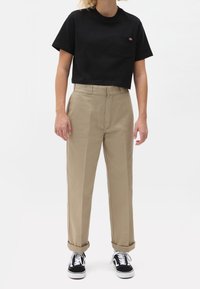 Black cropped t-shirt with a front pocket, beige high-waisted pants, and black sneakers with white soles. Smooth fabric, simple designs.