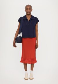 Marinblå kortermet polo med korte ermer, rød satengskjørt med utstående kant, hvite sokker og kremfargede sneakers. Tilbehør: liten crossbody-veske.
