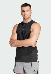 Ærmeløs atletisk sort skjorte med rund hals, lavet af letvægtsstof; har et diskret logo på brystet, parret med grå shorts.