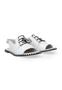 Hvite lædersko med åbne tæer, sorte snørebånd, sølvdetaljer og en stribet sort-hvid sål. Har et slingback-design.