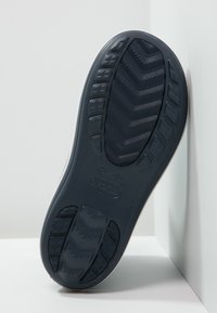 Semelle de chaussure en caoutchouc bleu foncé avec une texture antidérapante présentant un motif en zigzag et des bords arrondis, affichant le logo de la marque de manière proéminente.