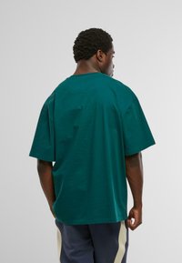 Tricou din bumbac verde, cu o croială relaxată, mâneci scurte și guler rotund. Textură netedă, cu un design minimalist, fără logo-uri vizibile.