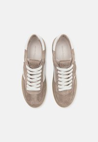 Une paire de baskets en daim beige avec des lacets blancs et des accents blancs au niveau du talon, vue du dessus sur un fond uni.