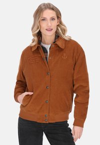 Bruine corduroyjas met drukknoopsluiting, zijzakken en een geborduurd ankerdetail op de linkerborst.