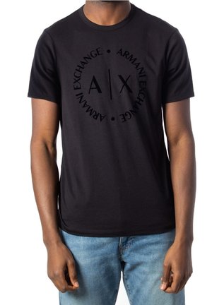 Homme portant un t-shirt noir Armani Exchange avec un logo circulaire de la marque et un jean bleu, montré du cou aux hanches.