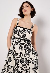 Robe noire à motifs floraux avec encolure festonnée et bretelles. Fabriquée en tissu léger, dotée de poches et d'un design fluide.