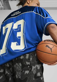 Blå atletisk trøje med hvide detaljer og nummeret "73" på ryggen; parret med mønstrede sorte shorts og en basketball med et logo.