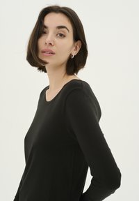 Fekete, hosszú ujjú felső, kerek nyakkivágással, puha anyagból készült. Testhez simuló szabású és sima textúrájú. Nincsenek látható minták vagy fémrészek.
