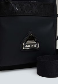Zwarte nylon schoudertas met een driehoekig zilveren logo plaatje en een geweven schouderband, voorzien van een ritssluiting en een textuur oppervlak.