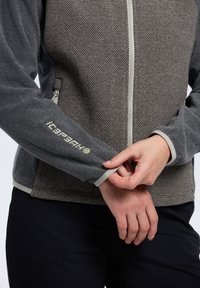 Harmaa vetoketjullinen takki, jossa on teksturoitu pinta. Ominaisuuksiin kuuluu vaaleanharmaat korostukset ja logo hihaassa. Slim fit -malli, jossa on sivutaskut.