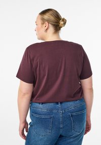 Burgundijas krāsas kokvilnas T-krekls ar īsām piedurknēm, apaļu kakla izgriezumu un brīvu piegriezumu, apvienots ar augsto vidukli ziliem džinsiem ar aizmugurējām kabatām.