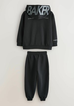 Sort hættetrøje med "BAKER" i reflekterende sølv på ryggen, kombineret med matchende sorte joggingbukser med manchetter. Blødt materiale.