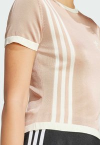 Ljusrosa stickad t-shirt med vit ribbad krage och manschetter, med tre vertikala vita ränder på vänster sida.