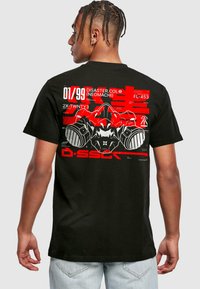 Sort T-shirt med rød grafisk design og tekst samt abstrakte elementer på ryggen. Korte ærmer, standard pasform og lavet af bomuld.