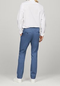 Hellblaue Baumwollhosen mit geradem Bein, zwei Gesäßtaschen und einem Knopfverschluss, kombiniert mit einem weißen Langarmhemd.