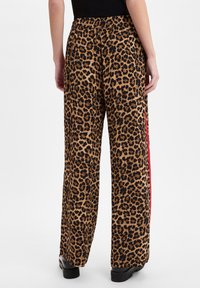Leoprint wijde pijpen met een zwarte elastische tailleband, contrasterende rode zijstrip en een soepele textuur.