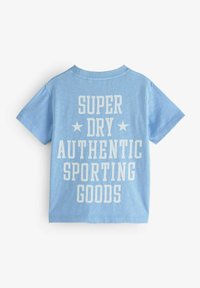 Sinine puuvillane T-särk, millel on suur valge tekst "SUPER DRY AUTHENTIC SPORTING GOODS" ning taga on tähed. Klassikaline sobivus.