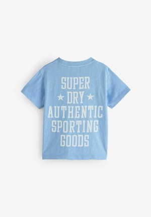 Mėlynas medvilninis T-palaidinukas su didelėmis baltomis raidėmis, kuriame užrašyta "SUPER DRY AUTHENTIC SPORTING GOODS", su žvaigždėmis ant nugaros. Klasikinis kirpimas.