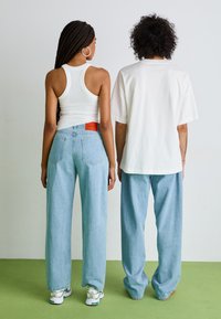 Deux personnes de dos portant un débardeur blanc à côtes et un t-shirt blanc surdimensionné, associés à un jean taille haute bleu clair.