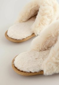 Faux fur slippers in cream color with a soft texture, featuring a braided golden sole and open back design for easy wear.