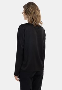 Maglietta nera a maniche lunghe con una texture liscia, caratterizzata da un colletto rotondo e una sottile cucitura sul retro. Abbinata a pantaloni neri.