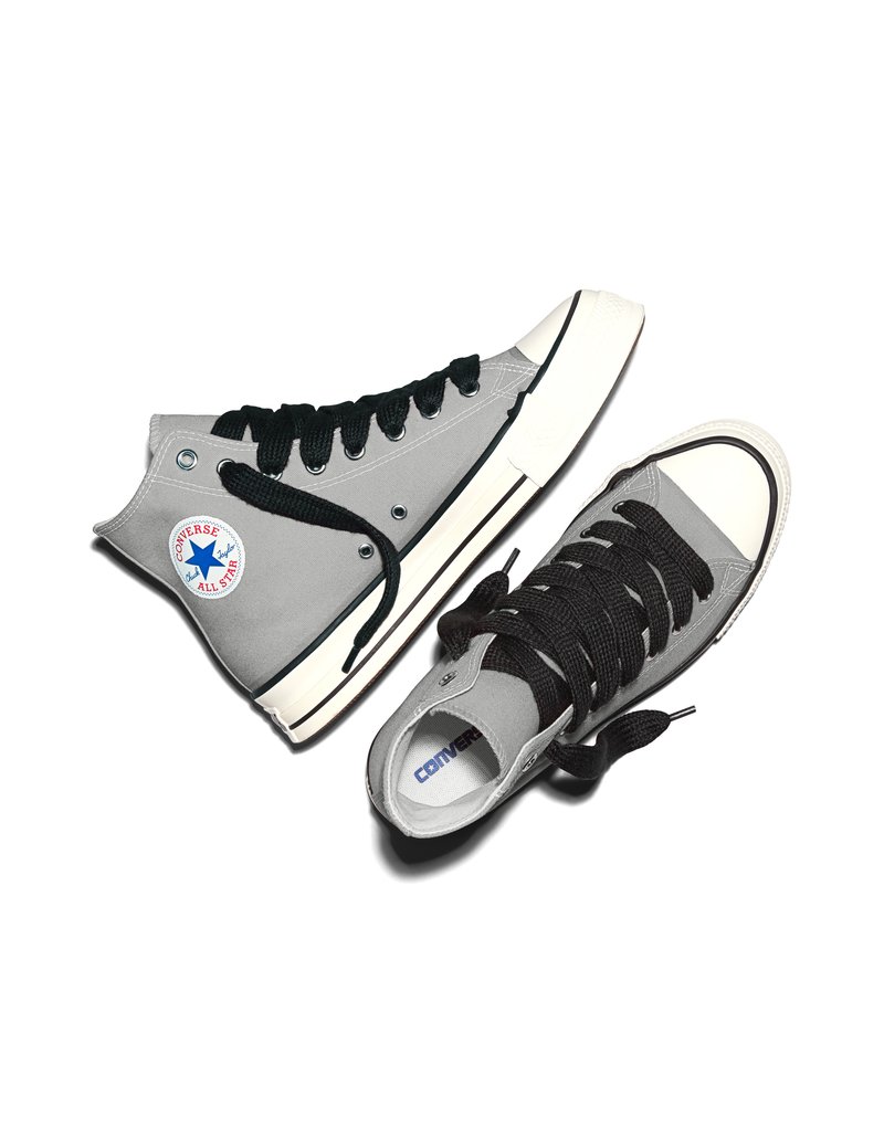 Scarpe da ginnastica Converse alte grigie con lacci neri e suole bianche, posizionate una accanto all'altra su uno sfondo bianco.